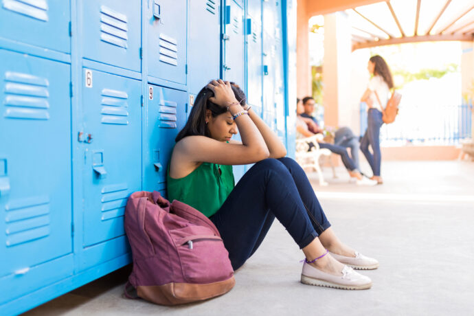 Teen sitting with her hands on her hair against lockers symbolizing anxiety in teens and the need for anxiety counseling.